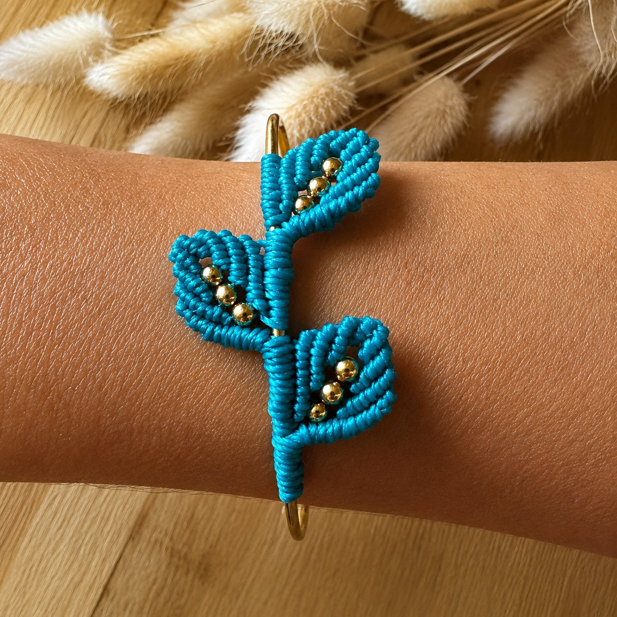 Bracelet jonc rigide en acier inoxydable avec tissage trois feuilles en micromacramé rose chamois et ses perles dorées.